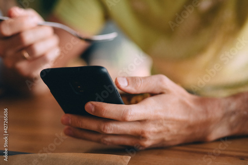 Guy using phone while eating, close view of hands using black phone © Ann