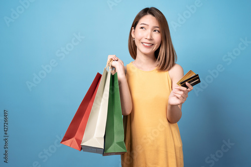 Young asian woman carrying shopping bags and credit card, Isolated on blue background.