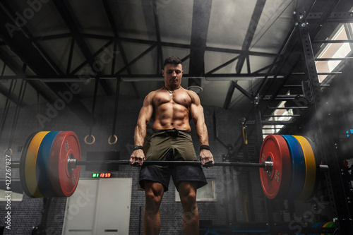 Weightlifter at the gym, a moment before a powerful movement. A man with a strong body holds a heavy barbell in his hands and does a dead lift in a dark atmosphere gym. Motivation in sports, cross fit