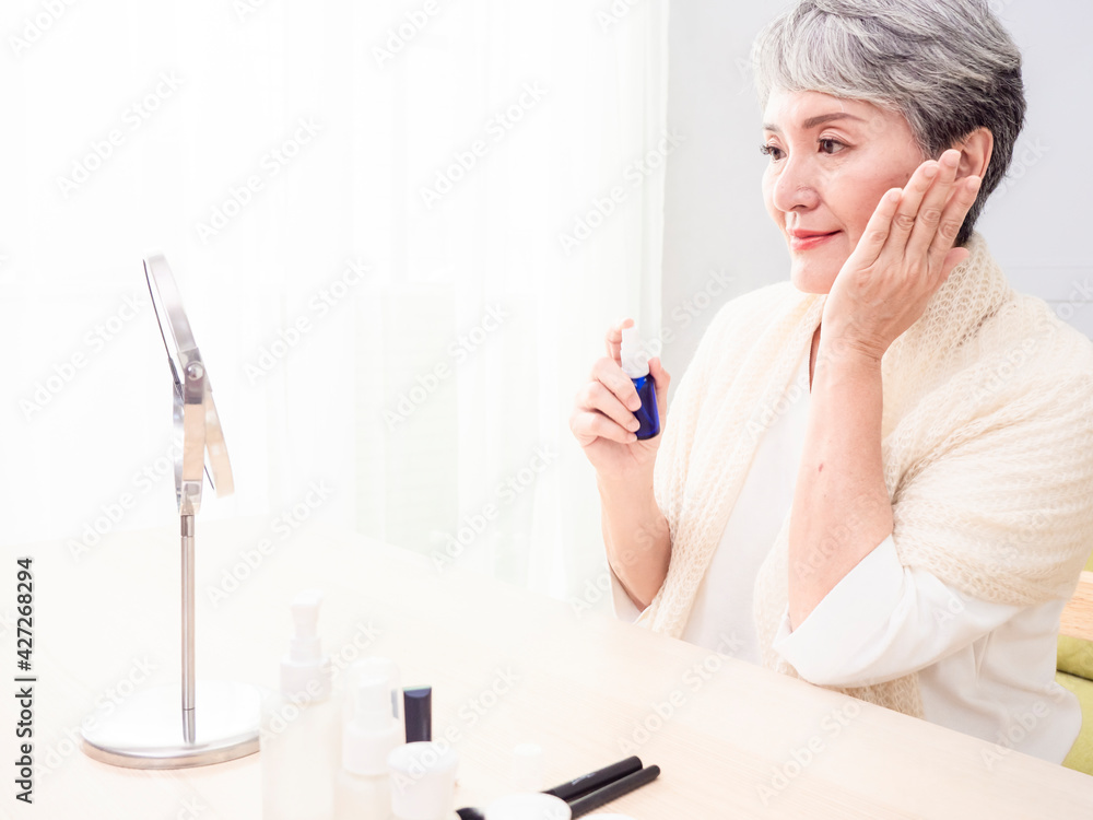 Happy senior asian woman applying lotion to her face. Happy senior asian woman applying lotion to her face.