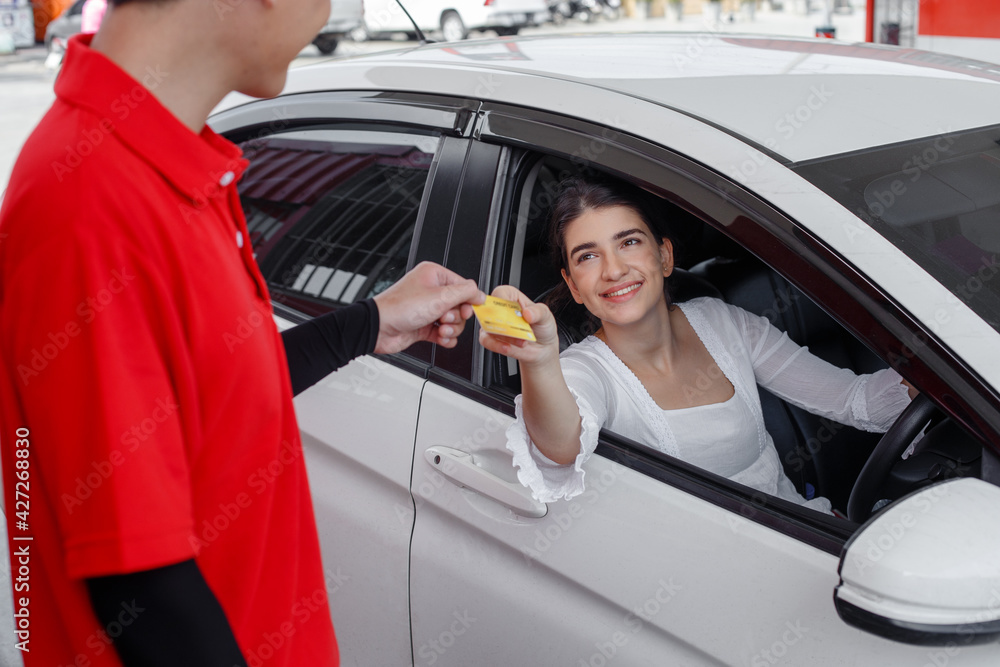 Naklejka premium woman in car paying credit card after refuel car ​spending instead of cash with man service employee at gas station. business finance energy concept.