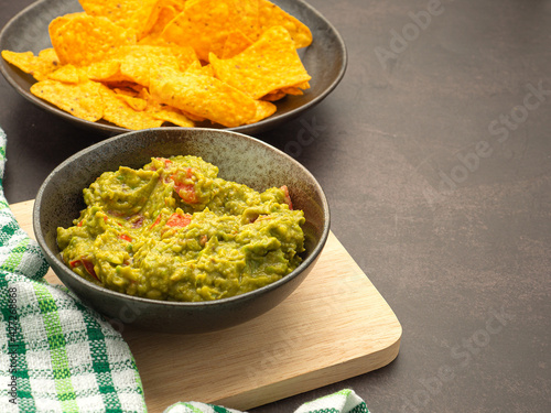 Fresh guacamole on a dish on a wooden cutting board and tortilla chips on a plate. Side view with copy space for text. Concept of healthy fruit and traditional Mexican foods