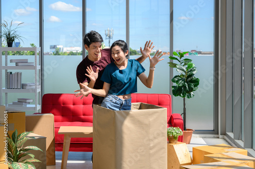 Happy young asian couple smiling relaxing and having fun while playing with cardboard box in new house, celebrating moving to new home concept