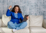 Young attractive woman sitting on the sofa in the room and operating a using browsing tablet computer on sofa at home, happy girl sitting on couch. Technology concept.