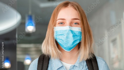 Happy smiling woman Schoolgirl in blue protective mask with backpack. Young woman student in medical mask. Portrait of blonde female student Girl at university interior during lockdow. Long web banner photo