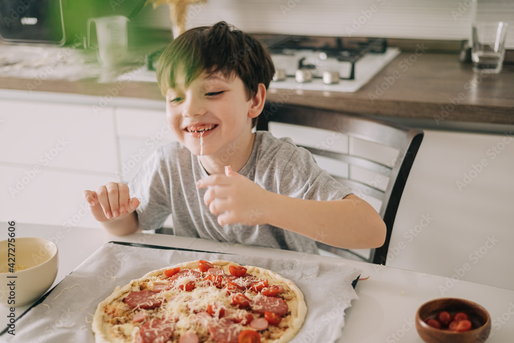 Little kid boy making pizza sitting at the table on the kitchen. Children helping in cooking lifestyle image Little kid boy making pizza sitting at the table on the kitchen. Children helping in cooking lifestyle image