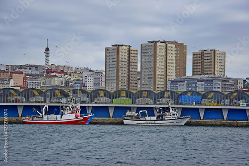 Barcos pesqueros en el puerto, tras los cuales hay edificios de almacenamiento y más allá grandes torres de apartamentos en la ciudad de La Coruña, España photo