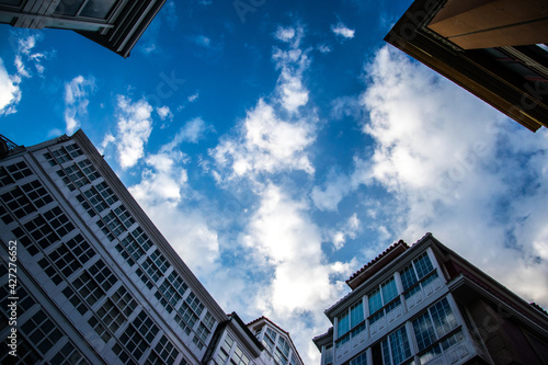 Imagen de ángulo bajo de la confluencia de varias fachadas y azoteas recortadas sobre el azul del cielo con nubes