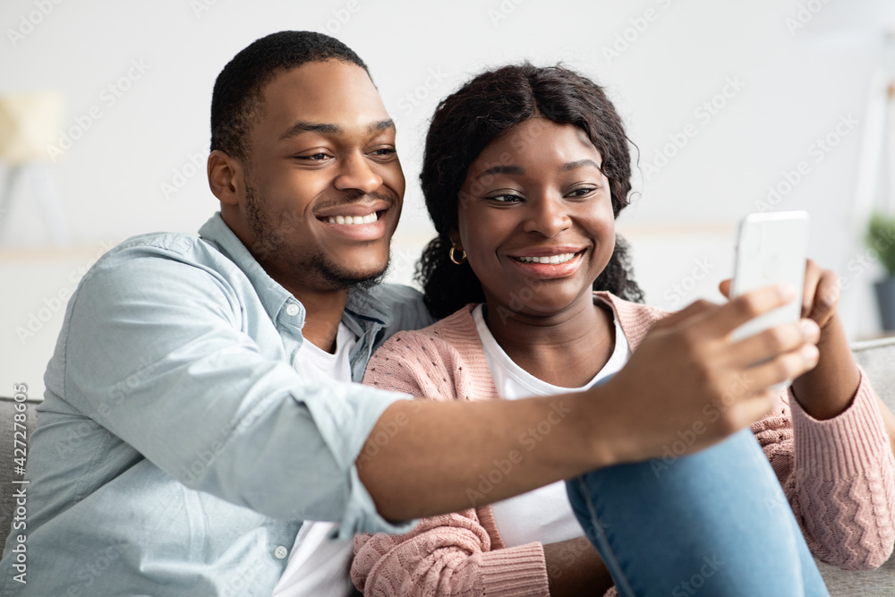 Cheerful african american couple taking selfie, using smartphone Cheerful african american couple taking selfie, using smartphone