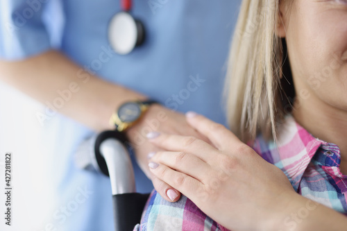 Nurse putting her hand on shoulder of young disabled woman in wheelchair closeup