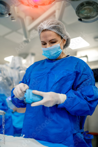 Focused surgeon in blue uniform and mask preparing for operation. Modern operation room in hospital.