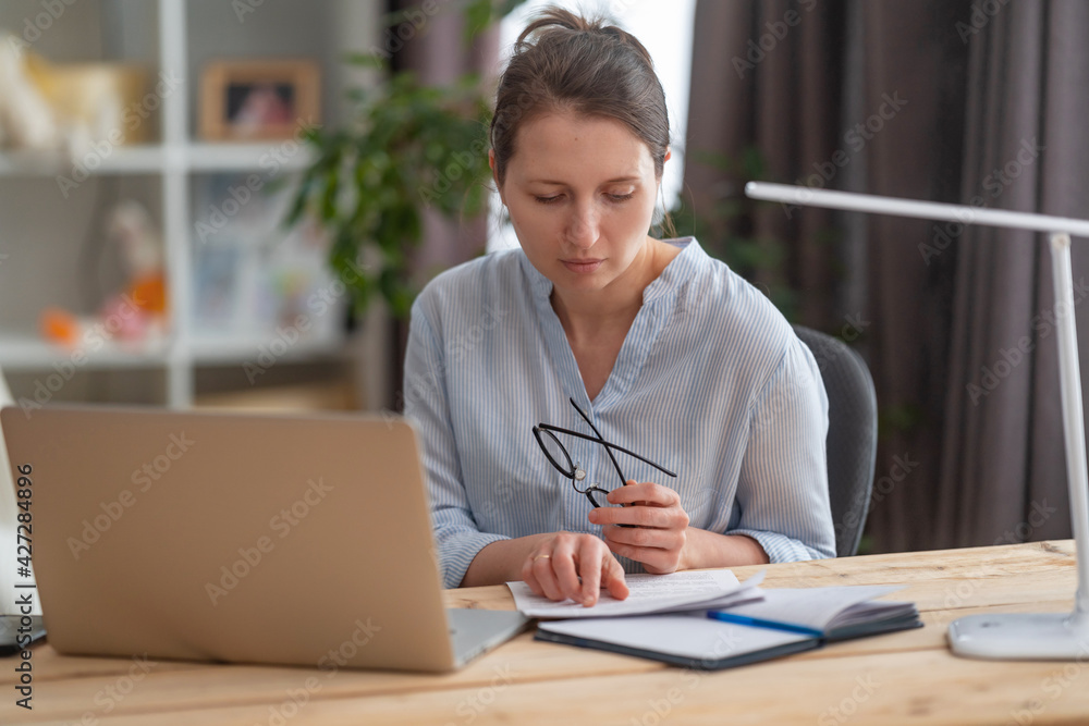 Focused young women sits at desk at home managers family household finance pay bills taxes on laptop online, modern housewife counts expenses, reviews financial documents. Freelancer, works from home Focused young women sits at desk at home managers family household finance pay bills taxes on laptop online, modern housewife counts expenses, reviews financial documents. Freelancer, works from home
