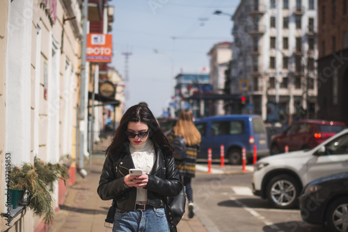 Young cheerful stylish woman using cell phone and texting message on city street © bisonov