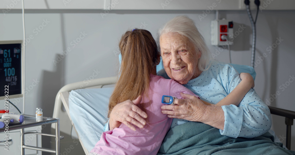 Little girl visiting and hugging sick grandmother in hospital ward