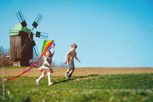 Happy kid boy and girl playing with kite over wind turbine farm and green renewable energy. Concept of sustainability development by alternative energy. Children and wind.