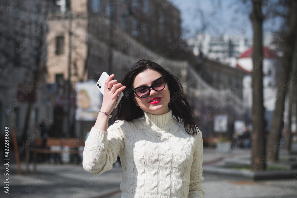 Young cheerful stylish woman using cell phone and texting message on city street Young cheerful stylish woman using cell phone and texting message on city street