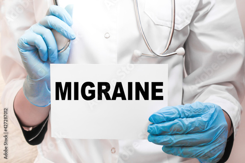 The doctor s blue - gloved hands show the word MIGRAINE - . a gloved hand on a white background. Medical concept. the medicine
