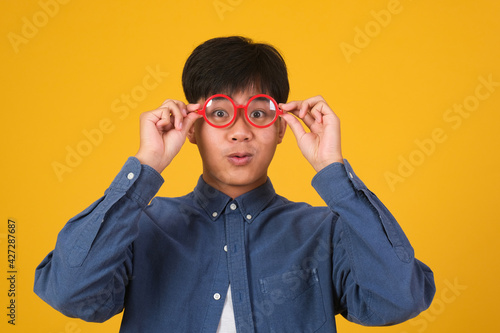 Portrait of asian nerd man with red glasses on yellow background.