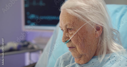 Close up portrait of sad and depressed sick aged woman lying in hospital bed photo