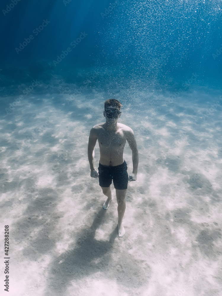 Fototapeta premium Sporty man freediver stay on sand bottom underwater in sea.