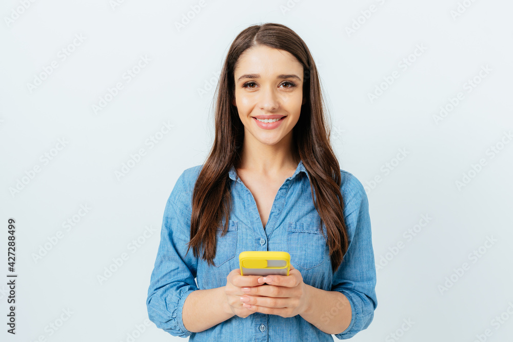 Happy young brunette woman wearing jeans shirt holding mobile phone Happy young brunette woman wearing jeans shirt holding mobile phone