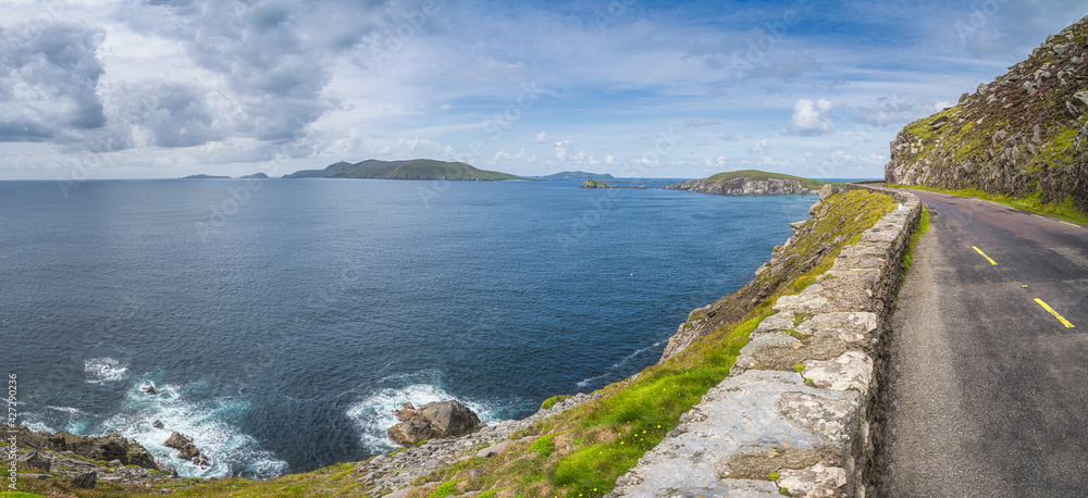 Large panorama with narrow winding road on the edge of cliff with archipelago of small islands in Dingle Peninsula, Wild Atlantic Way, Kerry, Ireland