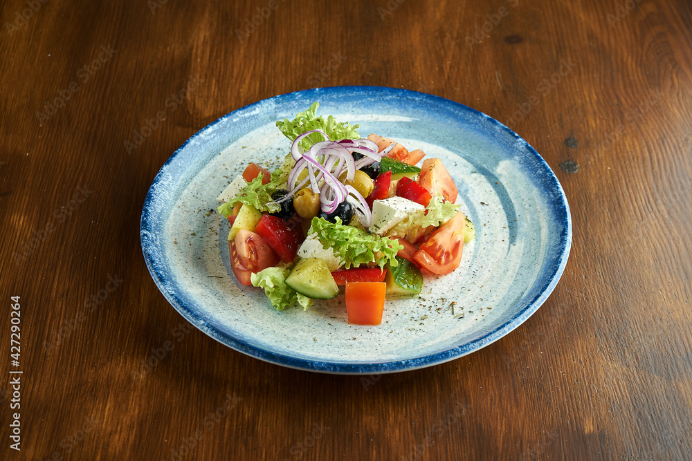 Classic Greek salad with tomatoes, cucumbers, red onions, feta cheese and olives, served in a blue plate on a wooden background. Classic Greek salad with tomatoes, cucumbers, red onions, feta cheese and olives, served in a blue plate on a wooden background.