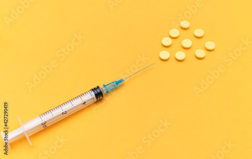 Syringe with a needle and pills on a yellow background. High dose, vitamin, yellow tablets coming out of the syringe needle. The concept of a vitamin complex, vitamins for health, beauty and youth. 
