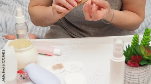 pretty girl using a cotton to removes her nail polish from her nails, next to there is hand cream, hand and nail care, self-care photo