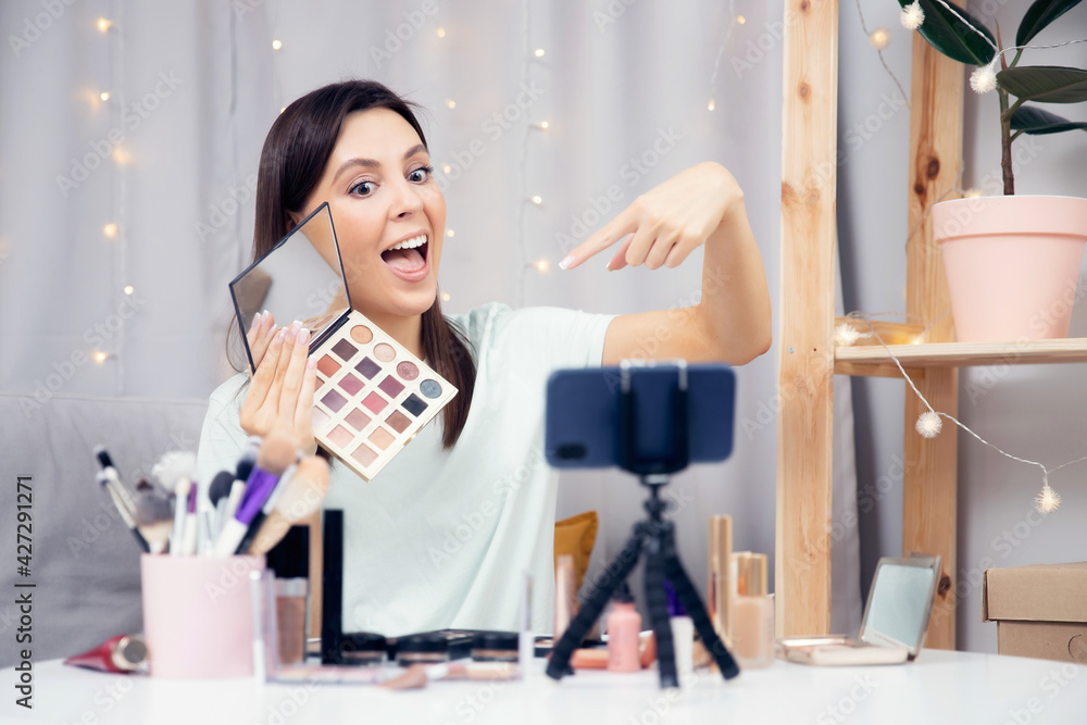 Concept Influencer blogger beauty blog. Happy woman vlogger is showing cosmetics products while recording video stream on phone Concept Influencer blogger beauty blog. Happy woman vlogger is showing cosmetics products while recording video stream on phone