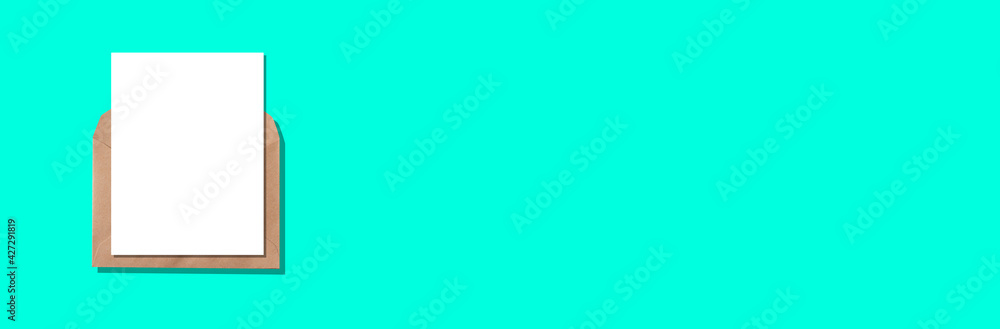 Obraz premium Empty blank white card with craft paper envelope template mock up on turquoise background. Flat lay, top view.