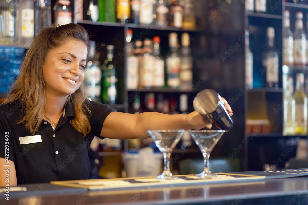 Professional bartender woman pours a fresh cocktail to the customers of the hotel bar. The bartender girl pours a cocktail. The concept of service. Focus on the bartender