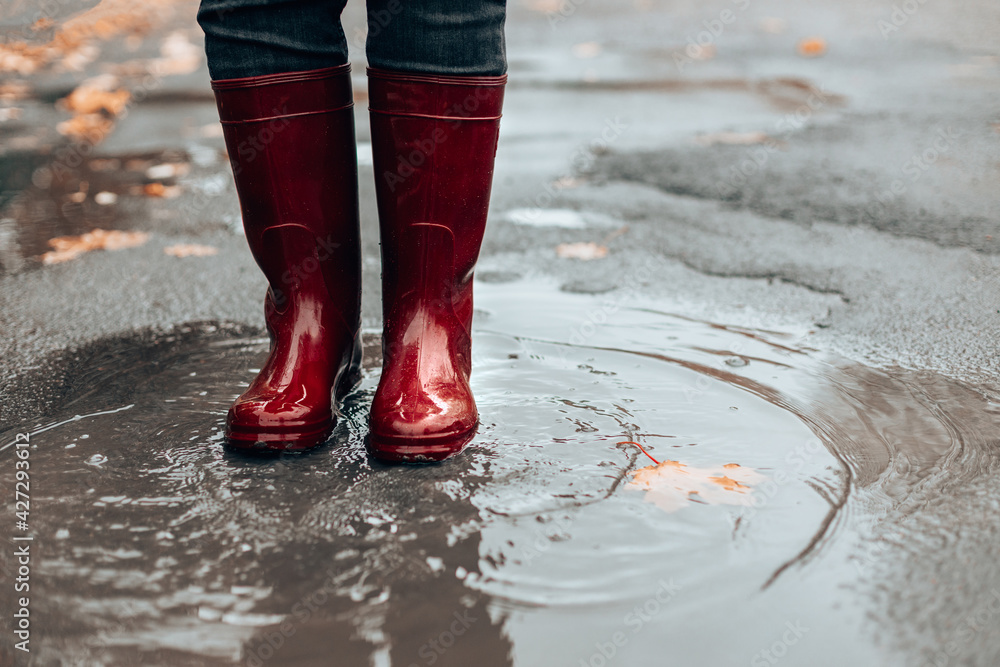 Woman with dark red rubber boots jumping in puddle, closeup. Rainy weather  Photos | Adobe Stock