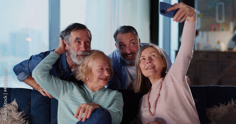Fototapeta premium Joyful family of four spending time indoors recording selfie video taking pictures having exciting leisure acrivities home entertainment on weekend.