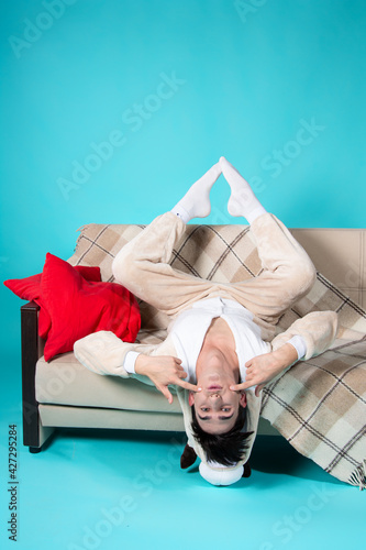 Funny student in pajamas with red pillows. A very emotional person. Relax on the couch before bed. Blue background.