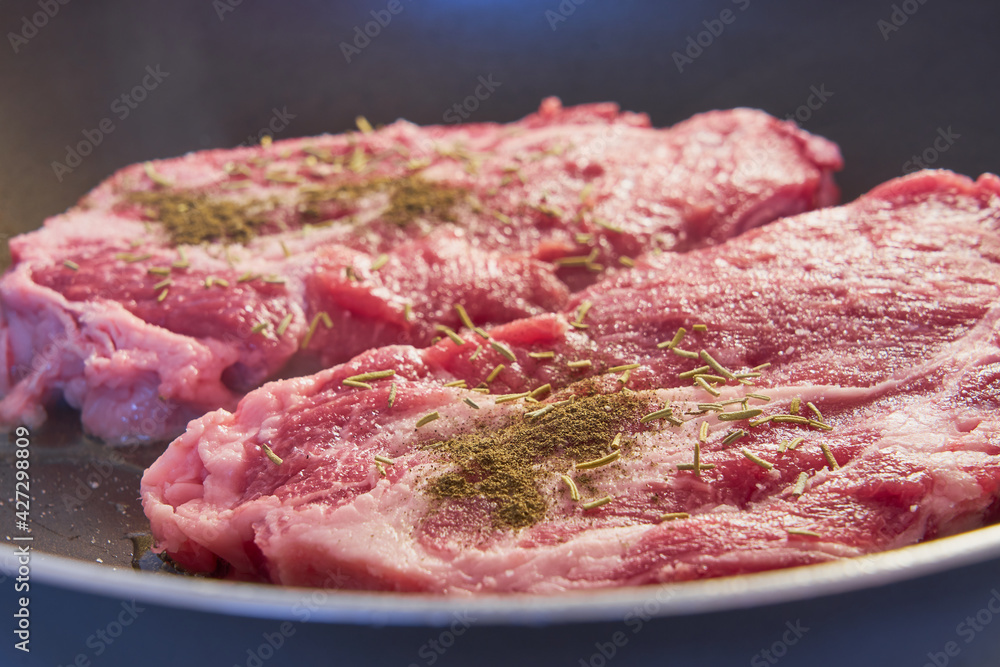 Two red meat steaks with spices in a frying pan. Two red meat steaks with spices in a frying pan.