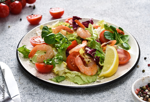 Mix salad with tomatoes and grilled shrimps with sauce and clematis on the kitchen table. Concrete food background.
