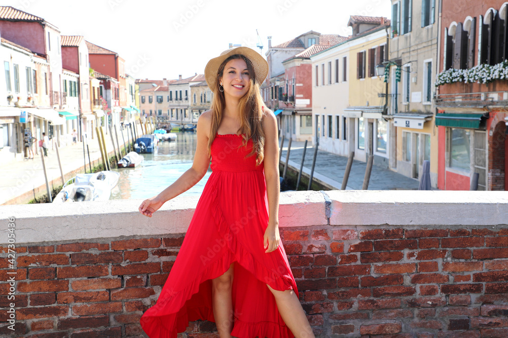 Elegant smiling fashion woman in red long dress on bridge in the old town of Murano, Venice, Italy