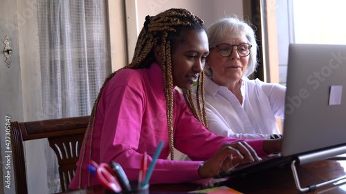 Young African woman teaching computer skills to an older woman with a computer in a house