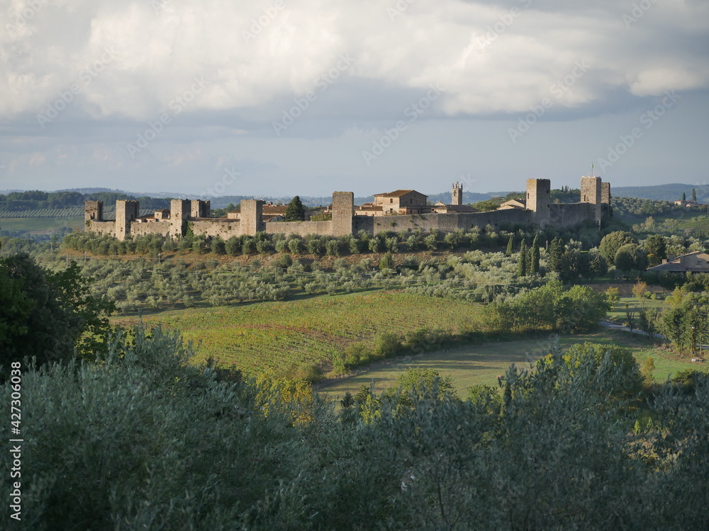 Panorama of Monteriggioni Castle with circular perimeter walls with 14 towers lying on the top of a hill surrounded by the countryside and olive groves