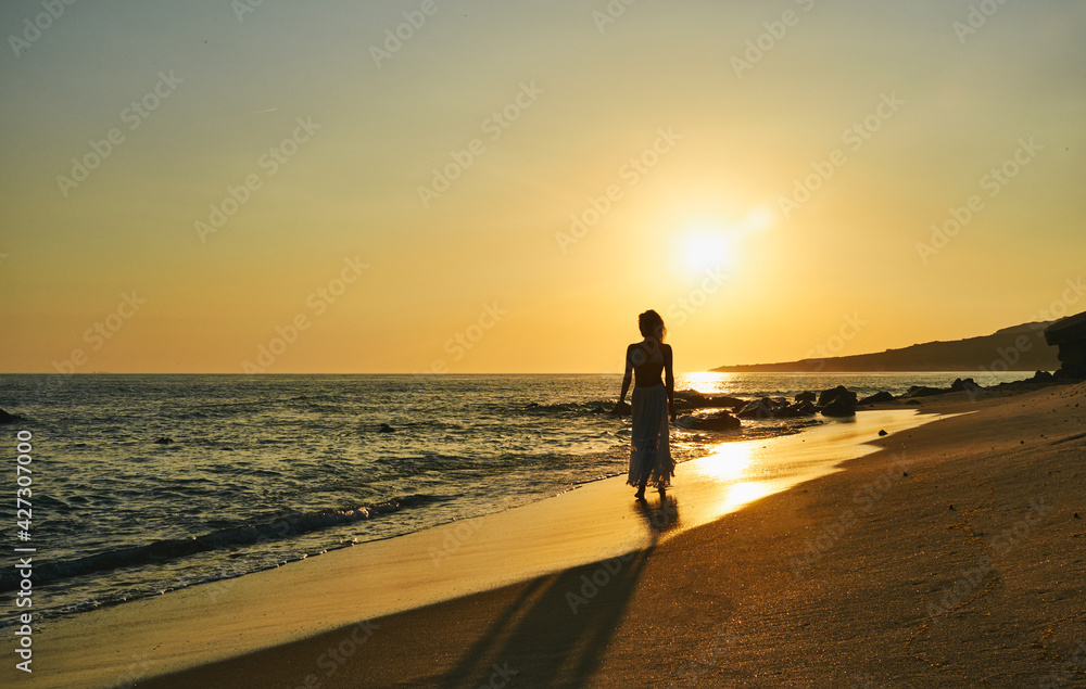 Carefree young woman walking along a sandy beach at sunset