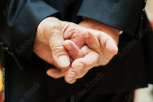 Hands clasped behind the back in close-up. Man is wearing a black suit. Wedding, birthday, metting or funeral? 