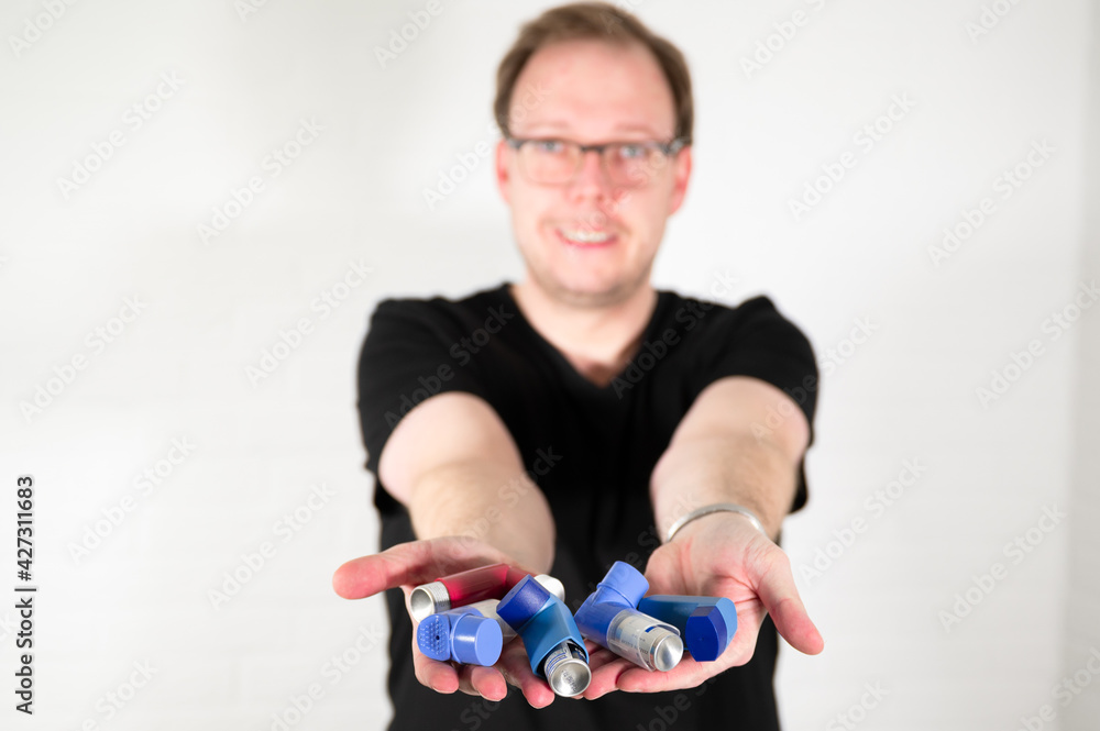 Man holding various red and blue asthma spray inhalers in his hand Man holding various red and blue asthma spray inhalers in his hand