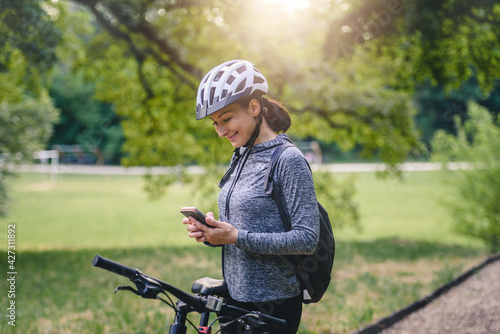 Smiling woman cyclist in the public park using a smart phone