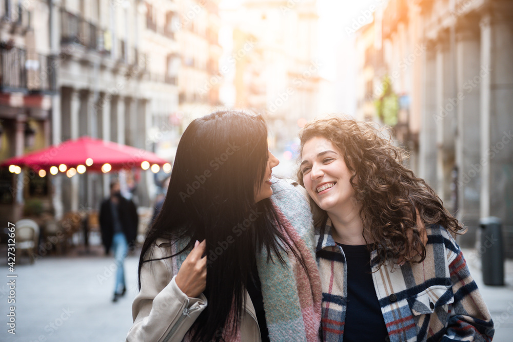 two girls walking, happy and laughing in the city. A couple of girls walk together. Women looking at each other and smiling.