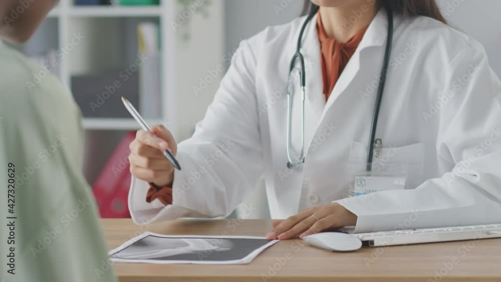 Female doctor or consultant wearing white coat having meeting with female patient in office to discuss x-rays or scans - shot in slow motion Female doctor or consultant wearing white coat having meeting with female patient in office to discuss x-rays or scans - shot in slow motion