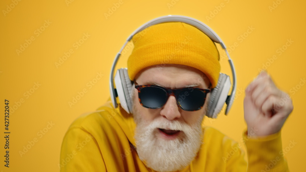 Happy senior man using headphones inside. Old guy moving to music indoors.