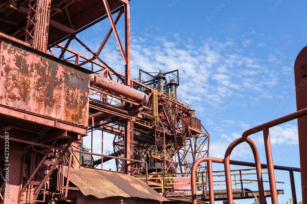 Expansive industrial steel manufacturing facility, rusted beams and girders, vivid blue sky, horizontal aspect