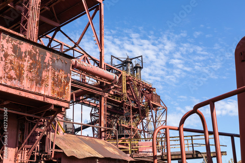 Expansive industrial steel manufacturing facility, rusted beams and girders, vivid blue sky, horizontal aspect