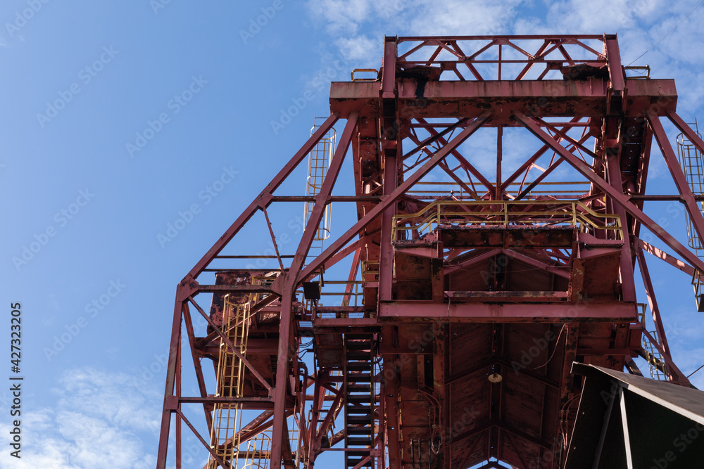 Huge rusting overhead industrial metal structure, caged ladders, blue sky, horizontal aspect Huge rusting overhead industrial metal structure, caged ladders, blue sky, horizontal aspect